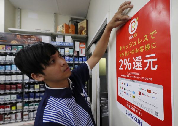 东京一家罗森便利店，店员正张贴海报，提示使用无现金支付的优惠返还活动